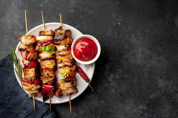 Meat skewers with grilled vegetables on a white plate on a stone background with copy space for your text