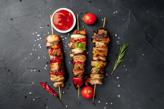 Meat skewers with grilled vegetables on a stone background
