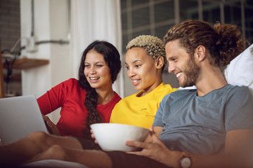 Happy friends relaxing in bed at home watching a movie on laptop