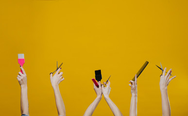 Three sets of woman hands in the air holding hairdresser tools over yellow