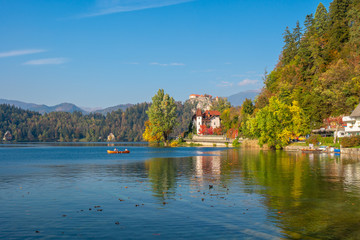 Fototapeta na wymiar BLED, SLOVENIA - October 9, 2018: Beautiful view on lake with boats surrounded by hills with castle on top on clear sunny autumn day. Travel destinations landscapes concept
