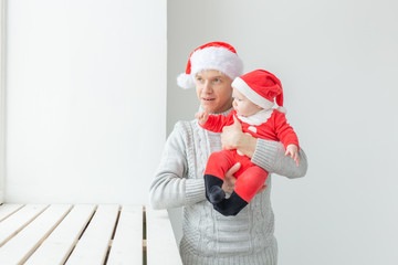 Obraz premium Fatherhood and holidays concept - Father with his baby boy wearing Santa hats celebrating Christmas