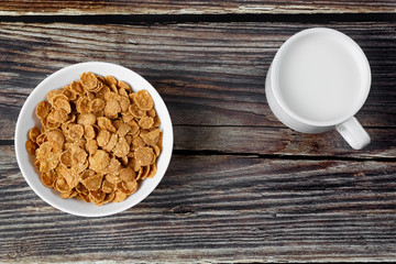 White plate with healthy cereal breakfast and cup of milk on a wooden surface.