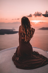 Young woman with blonde hair and purple dress watching the sunset in santorini greece