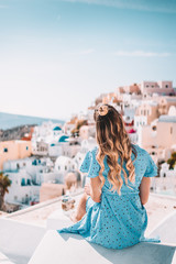 Fototapeta na wymiar Young woman with blonde hair and blue dress in oia, santorini, greece with ocean view and churches