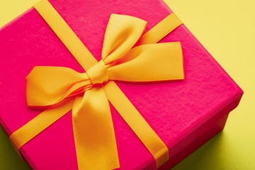 Close-up of a purple gift box with a yellow ribbon tied with a bow on a yellow background