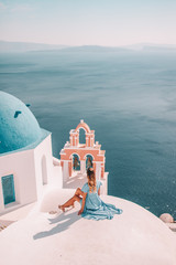 Young woman with blonde hair and blue dress in oia, santorini, greece with ocean view and churches