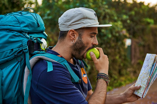 Backpacker biting an apple and checking his map