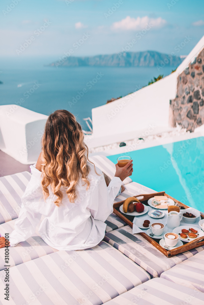 Wall mural woman having breakfast by the pool in santorini, greece