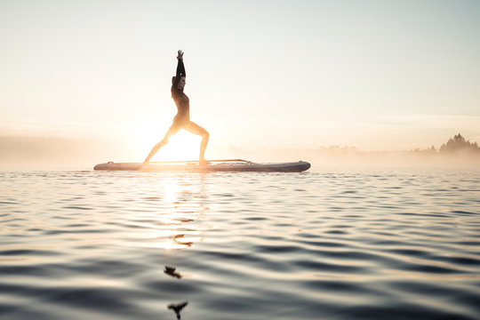 Woman practicing paddle board yoga on lake Kirchsee in the morning, Bad Toelz, Bavaria, Germany