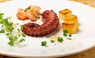 Grilled octopus on white restaurant plate served with shrimps