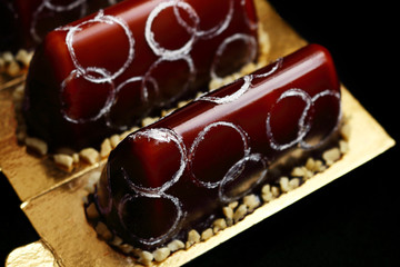 Two chocolate fancy desserts with chocolate mirror glaze peanuts and silver circles decoration top view