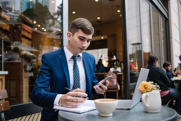 Serious businessman using smartphone and making notes outside bakery