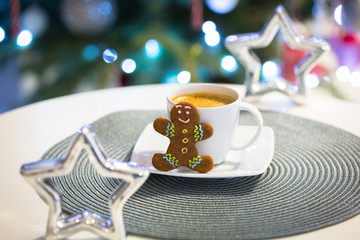 Gingerbread cookie man at the cup of hot coffee and christmas tree lights in background