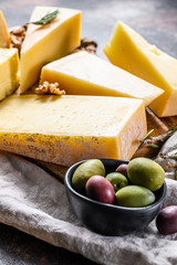 Different kinds of cheese, olives and rosemary. Assorted delicious snacks. Dark background. Top view