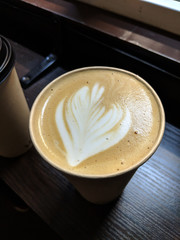 Cup of fresh latte drink decorated with heart shaped foam silhouette on dark wooden table in coffe to go spot