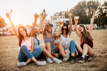 Group of female friends cheering with beer and having fun at music festival