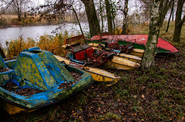 Old boats and catamarans are rusting in the open. Dump in the forest at the foot of the river bank...