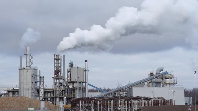 An industrial zone with large chimney, thick white smoke pours out of factory chimney at sunset, against background of thick clouds. Environmental pollution: smoke pipe. Seamless cinemagraph video.