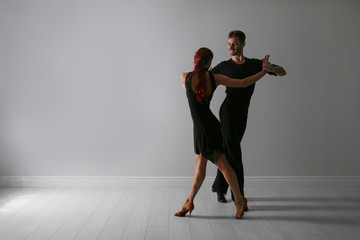 Beautiful young couple dancing near light wall. Space for text