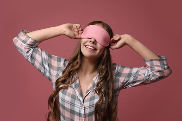 Young woman wearing pajamas and sleeping mask on dusty rose background. Bedtime