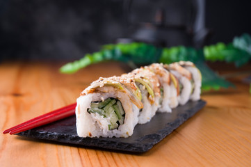 Sushi rolls with grilled eel, avocado, cucumber and cream cheese inside. Philadelphia roll with fish on a black background and a Japanese teapot and cups. Sushi menu. Japanese food. Horizontal photo.