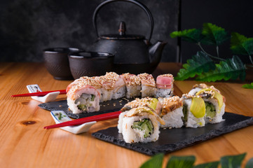 sushi roll with bacon, grilled eel, avokado red chopsticks, soy sauce, top view, sushi menu. Japanese food, on a black background and a Japanese teapot and cups.