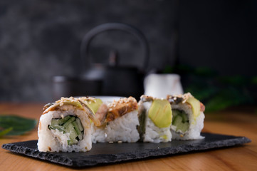 Sushi rolls with grilled eel, avocado, cucumber and cream cheese inside. Philadelphia roll with fish on a black background and a Japanese teapot and cups. Sushi menu. Japanese food.
