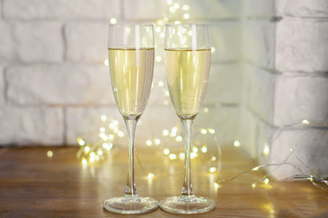 Celebratory glasses with champagne on a New Year's table. Background for christmas or new year with garland and bokeh. A romantic evening.