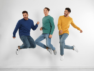 Fototapeta na wymiar Group of young men in stylish jeans jumping near white wall