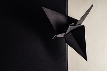 origami crane made of dark gray paper stands on sheets of paper