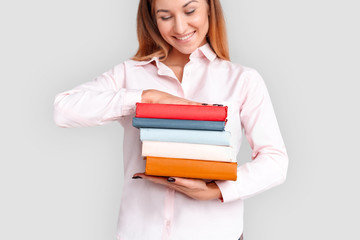 Freestyle. Young woman student standing isolated on white with books looking down smiling happy
