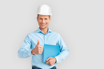 Construction. Mature man in hardhat standing isolated on white with clipboard thumb up smiling cheerful