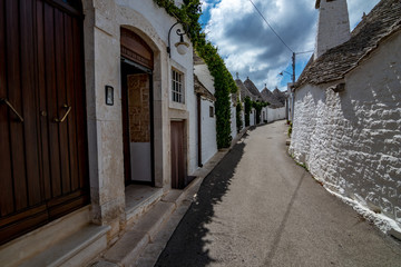 Narrow street with roofs and entrances of truli, typical whitewashed cylindrical houses in Alberobello, Puglia, Italy with amazing blue sky with clouds, street view