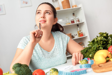 Body Care. Chubby girl sitting at kitchen table writing meal plan smiling thinking close-up