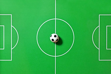 Top view of a foosball table. Toy soccer ball  in center of the green field, midfield