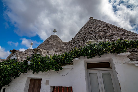 Roofs of truli, typical whitewashed cylindrical houses in Alberobello, Puglia, Italy with amazing blue sky with clouds and Sun shining