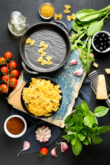 Pasta ingredients. Cherry tomatoes, farfalle pasta, garlic, basil, parmesan, spinach, arugula, spice and olive oil an on a dark background