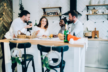 Cheerful group of friends eating and drinking in kitchen celebrating Christmas holiday at home