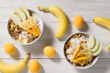 Two plates with oatmeal and cups of cornflakes and puffed rice on a white wooden background