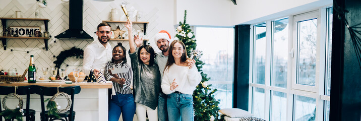 Cheerful group of young friends posing with props enjoying Christmas weekend party at home
