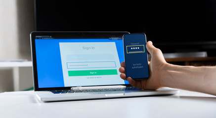 holding a phone and working using laptop, log in on website, double-factor authentication interface