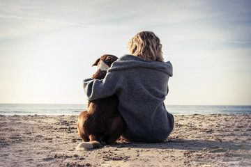 Young woman sitting and hugging dog on the beach. Friendship concept - woman and dog sitting...