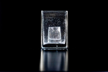 Small glass stands at bottom of large glass filled with carbonated liquid. Symbol of problem of alcoholism.