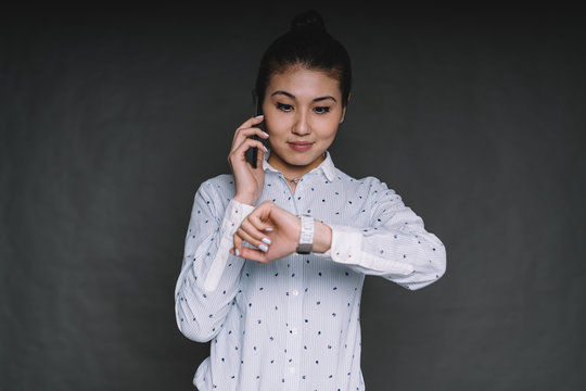 Pleased Asian woman checking time talking on smartphone - Powered by Adobe