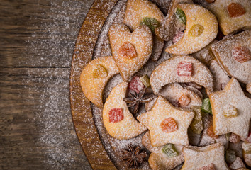 Homemade cookies in heart, moon, star shapes on wooden table on round wooden vintage plate decorated with candied fruit, icing sugar and star anise. Christmas food festive background. Text space.