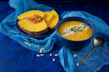 pumpkin cream soup in a blue plate on a deep classic blue background with slices of pumpkin with blue gauze and a spoon
