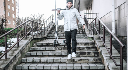 man in winter clothes carries an electric scooter up the steps.