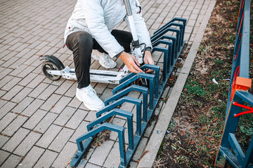 man hangs a cable lock on an electric scooter in a bicycle parking lot. Protection against theft of vehicles.