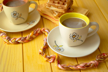Cocoa drink in yellow and orange mugs on wooden bright yellow background